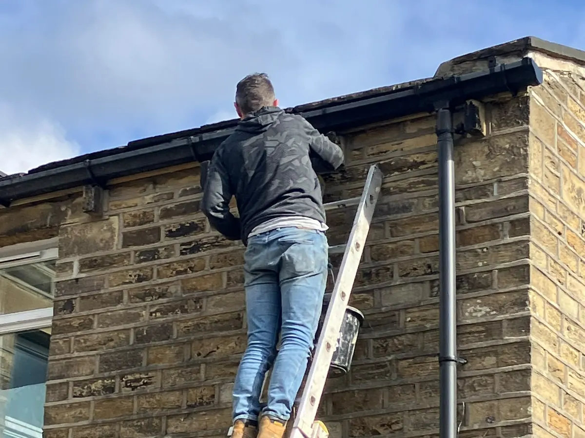 Roofer up a ladder working on the gutter line of a Halifax stone property