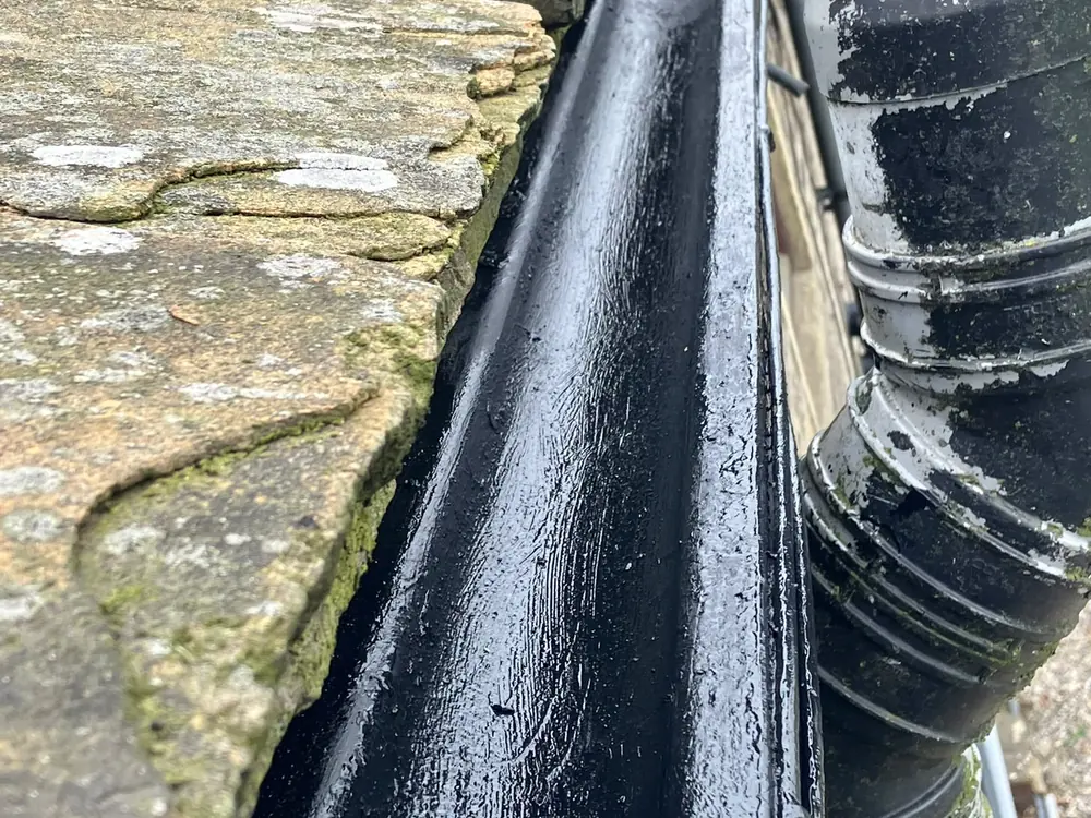 Cleared and repainted cast-iron gutter running along a stone roofline