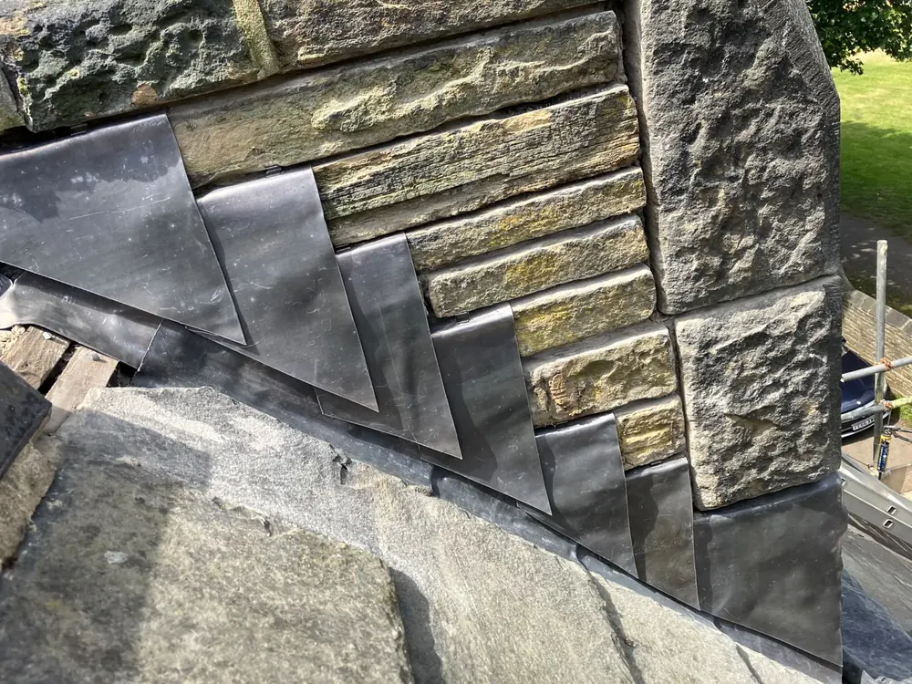 Lead flashing and felt detailing where a flat roof meets a stone wall